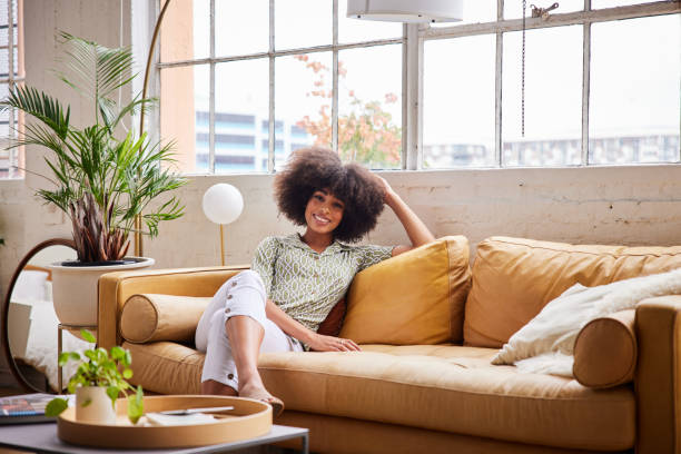 Smiling young woman relaxing on a comfortable sofa at home in the afternoon stock photo