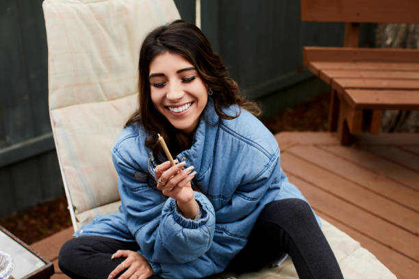Smiling young woman smoking a joint outside Young woman laughing while sitting alone outside on her patio and smoking a joint marijuana herbal cannabis photos stock pictures, royalty-free photos & images