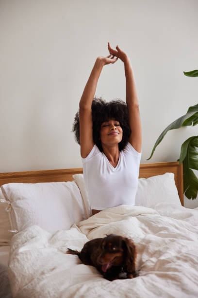 Smiling young woman stretching while waking up with her dog in the morning stock photo
