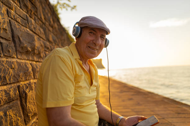 smilling cute senior man listening music and enjoying sunset - senior listening music beach bildbanksfoton och bilder