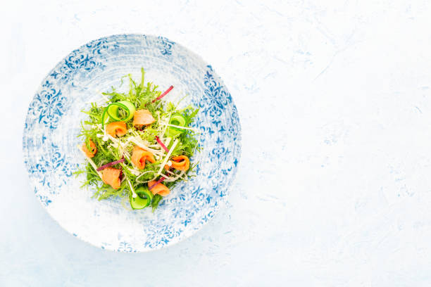Smoked salmon salad with Arugula, apple, enoki mushrooms, zucchini and beetroot on a white and blue plate over a blue background with copy space. stock photo