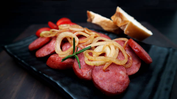Smoked sausage with bread and onions on dark background. Snack appetizer calabrese sausage. stock photo