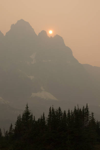 An orange sun sinks towards the Ramparts in a smoky sky filled with smoke from British Columbia wildfires.