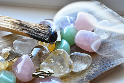 A close up image of burning wooden incense with small polished healing crystals.