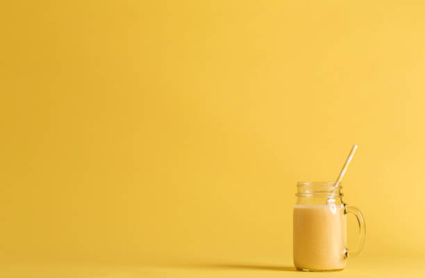 Smoothie in a mason jar Smoothie in a mason jar on a yellow background mango smoothie stock pictures, royalty-free photos & images