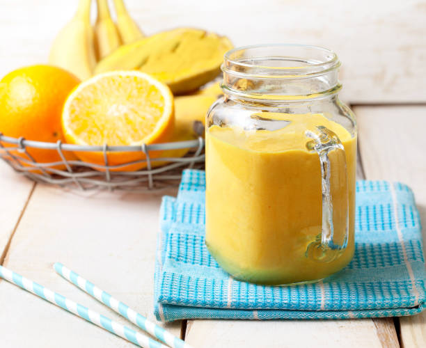 smoothie smoothie of banana, orange, mango in Mason jar on a wooden background orange smoothie stock pictures, royalty-free photos & images