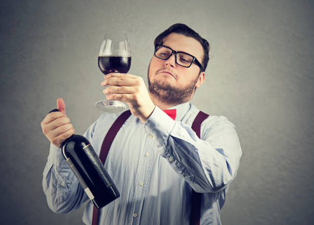 Snobby wine expert exploring drink Chubby man in wearing eyeglasses and bow tie holding wineglass and judging drink quality looking overconfident. snob stock pictures, royalty-free photos & images