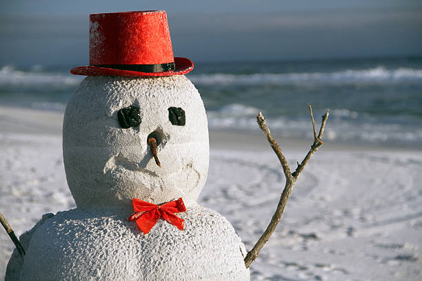 Snow Christmas snowman in santa hat at sandy beach stock photo