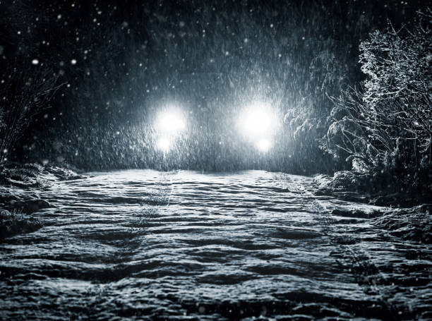 Snow falls on the road in the headlights stock photo