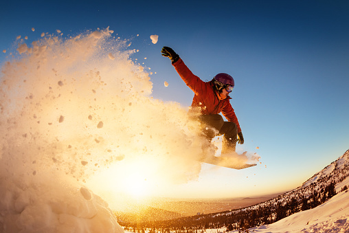 Snowboarder jumps sunset with snow dust