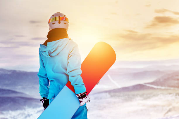 Snowboarder woman girl sunrise mountain top Girl snowboarder stands with snowboard on mountain's top on sunrise backdrop. Sheregesh ski resort boarding stock pictures, royalty-free photos & images