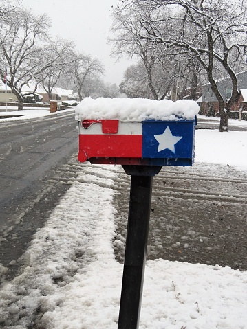 A mailbox painted in Texas flag covered with snow beside a Texas road on January 2021. Copy Space.