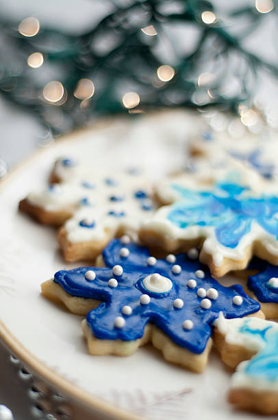 Plate of holiday season (Christmas or Hanukkah) snowflake shaped sugar cookies with white Christmas lights in the background.