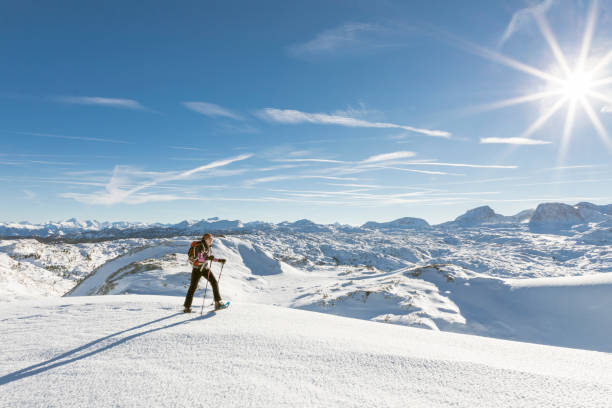 Snowshoeing on a sunny day at Dachstein Mountains, Austria. A lonely female is crossing a snowfield with snowshoes in front of the scenic Dachstein Mountains on a sunny winter day.
 dachstein mountains stock pictures, royalty-free photos & images