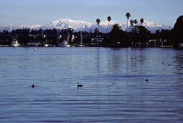 Snowy San Gabriel Mountains and Newport Bay, 1980 Rare snowcapped San Gabriel mountain range rises in the distance beyond the tranquil Newport Bay. Deeply-shadowed boats and bay-side properties in the foreground. hearkencreative stock pictures, royalty-free photos & images