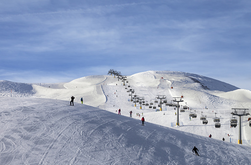 Snowy ski track prepared by snowcat, chair-lift, skiers and snowboarders in ski resort