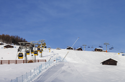Snowy ski track prepared with snow grooming machine, gondola lift, chair-lift