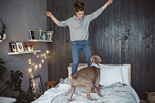 Young women and her dog in bedroom. They jumping on bed and enjoy in weekend together