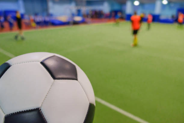 soccer ball on stadium and football players defocused in field - futsal imagens e fotografias de stock