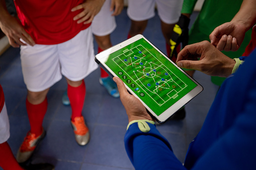 Close-up on a soccer coach talking to his team about the lineup for the game and using a tablet computer - sports concepts