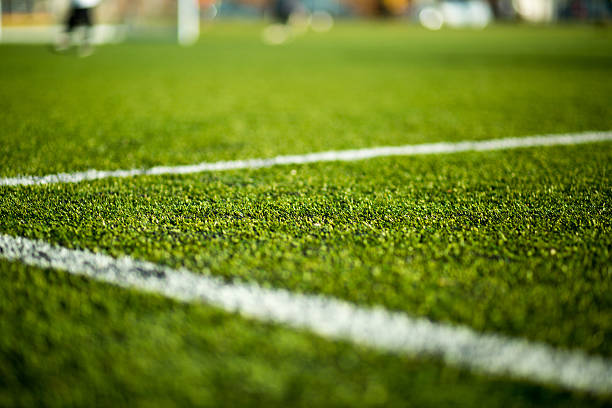Soccer pitch Close-up of artificial turf. Blurred legs of soccer players in the background. sports field stock pictures, royalty-free photos & images