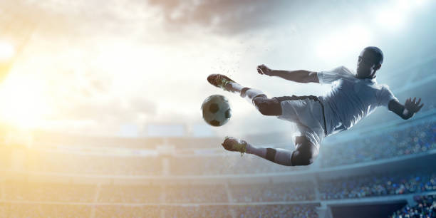 Soccer player kicking ball in stadium A male soccer player makes a dramatic play by jumping horizontally. He attempts to kick the ball with his feet. The stadium is blurred behind him. Only the lights of the stadium shine brightly, creating a halo effect around the bulbs. kicking stock pictures, royalty-free photos & images