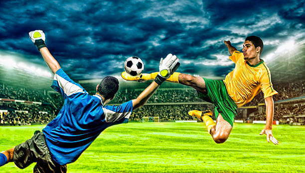 Soccer player kicks football in the air Soccer player jumps thorugh the air and kicks a ball. Goalkeeper tries to block the shot. Stadium in the background.  soccer striker stock pictures, royalty-free photos & images