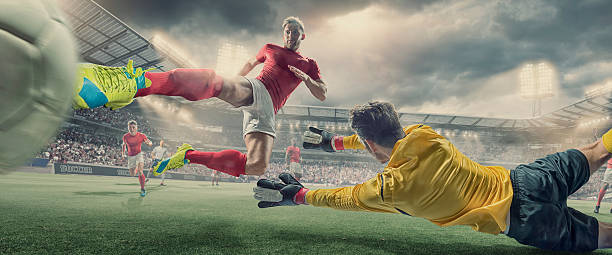 Soccer Player Scores Goal With Volley Kick In Football Match A close up view of a professional soccer player in dramatic mid air pose, kicking the football in a volley to score past a diving goalkeeper. The action takes place during a football match in a fictional floodlit outdoor stadium full of spectators under a dramatic stormy evening sky.  soccer striker stock pictures, royalty-free photos & images