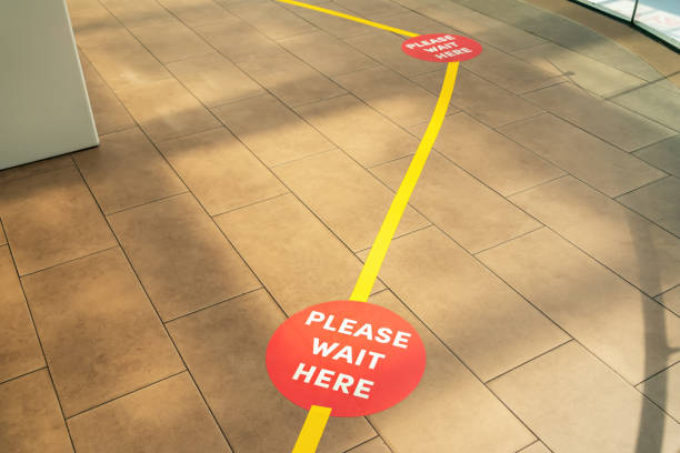 Social Distance Shopping Line Up. Secure marking yellow tape lines on floor for waiting in store. Please wait here stock photo