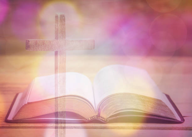 Soft focus of wooden cross over opened bible on wooden table with bokeh light. stock photo