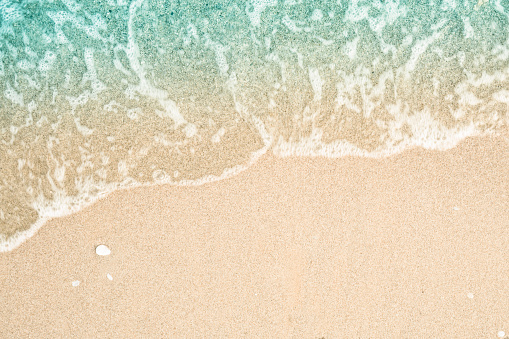 Soft wave of turquoise sea water on the sandy beach. Close-up and directly above photographed.