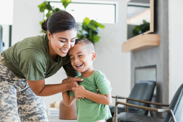 Solder embraces young son A cheerful female soldier smiles as she embraces her little boy while relaxing at home. tickling beautiful women pictures stock pictures, royalty-free photos & images