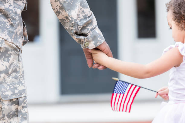 Soldier and his daughter walk hand in hand Unrecognizable soldier walks hand in hand with his preschool age daughter upon his return home from deployment. The girl is holding an American flag. soldiers returning home stock pictures, royalty-free photos & images