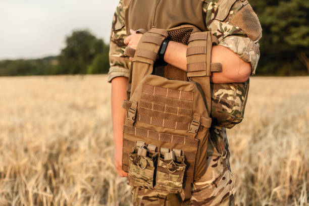 Soldier man standing against a field Soldier man standing against a field. Soldier in military outfit with bulletproof vest. Photo of a soldier in military outfit holding a gun and bulletproof vest on orange desert background. armored clothing stock pictures, royalty-free photos & images