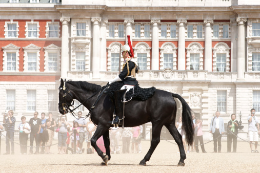 London, United Kingdom - July, 3rd 2010:  Royal Guard solider on horse in front of Buckingham Palace and tourists crowd preforming changing of the Guard. Passing horses raised dust from the ground.