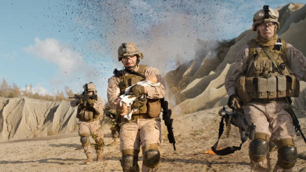 Soldier Running away from Explosions behind Carrying a Baby. While other Members of the Squad Covering Them During Battle in the Desert. Soldier Running away from Explosions behind Carrying a Baby. While other Members of the Squad Covering Them During Battle in the Desert. afghanistan stock pictures, royalty-free photos & images