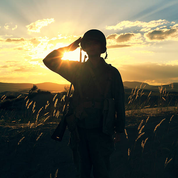 A World War 2 army soldier saluting with sunset behind him. Authentic WW2 army uniform.