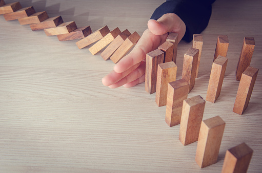 Closeup image of a finger try to stopping falling wooden dominoes blocks for business solution concept
