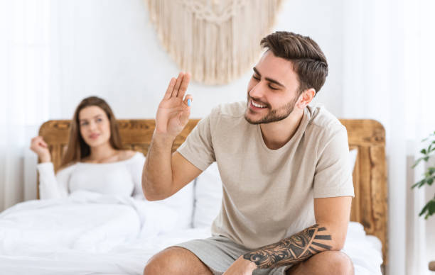 Solving problems in bed. Smiling man holding in hand blue pill, woman looking at husband Solving problems in bed. Smiling man holding in hand and looking at blue pill, happy woman looking at husband in bedroom interior, free space anti impotence tablet stock pictures, royalty-free photos & images