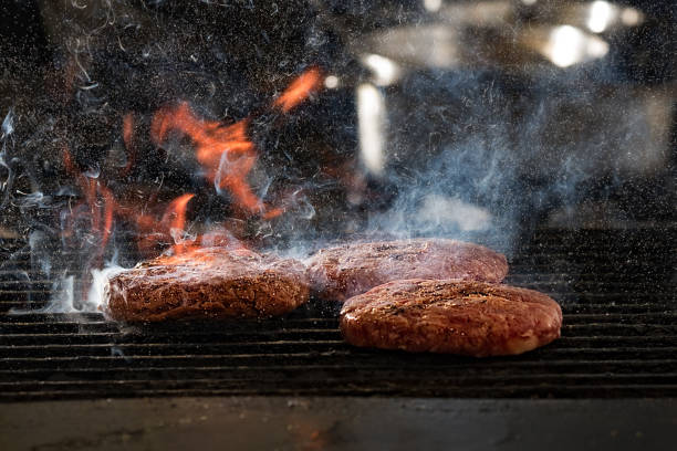 Some patties of ground meat with a flame in the front on cooking grate stock photo