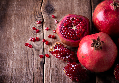 Some red juicy pomegranate, whole and broken, on dark rustic wooden table