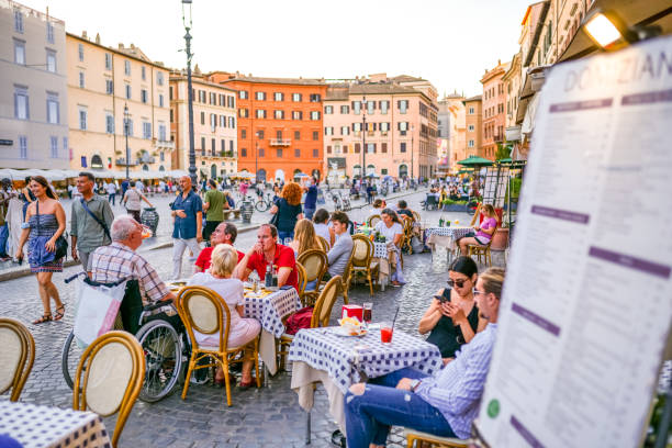 some tourists enjoy life sitting in a outdoor cafe in piazza navona in the baroque heart of rome - focus un focus stockfoto's en -beelden