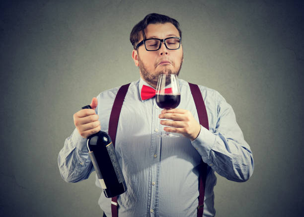 Sommelier smelling wine in glass Concentrated man holding bottle of wine and smelling beverage with eyes closed on gray backdrop. snob stock pictures, royalty-free photos & images
