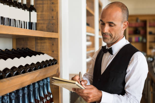 Sommelier writing inventory Sommelier writing inventory for red wine in stock in a shop. Multiethnic man taking notes in winery with wine bottles stacked in rows on the shelves. Bartender writing on a notebook."r waiter taking order stock pictures, royalty-free photos & images