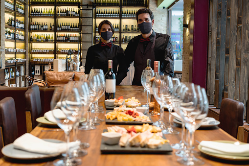 Team of sommeliers hosting a winetasting event at a cellar wearing facemasks during the COVID-19 pandemic