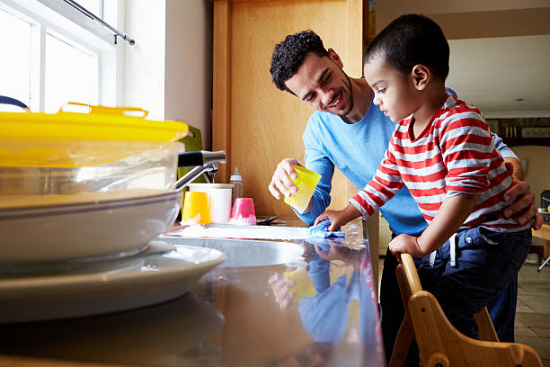 Son Helping Father To Wash Dishes In Kitchen Sink stock photo