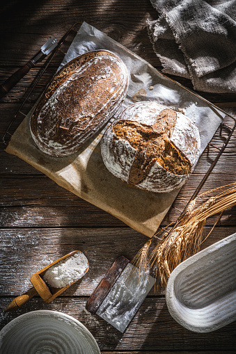 Sourdough bread loaf and Banneton basket in bakery on wooden rustic table and with bread loaves in background