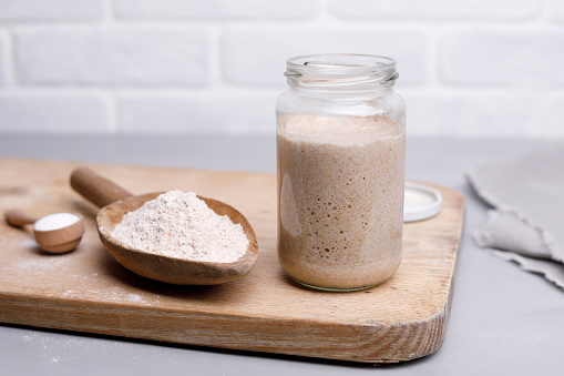 Active rye sourdough in glass jar and flour in wooden spoon.