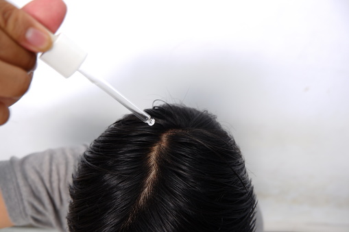 Southeast asian man dropping serum onto his hair, top view