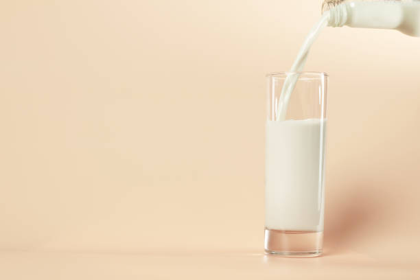 Soy milk in the glass by pouring from bottle as pastel orange colors background. Healthy food and vegetarian concept. stock photo
